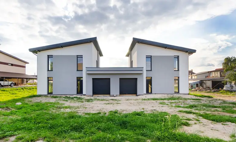 Two newly built modern family homes with pitched metal roofs under a clear sky