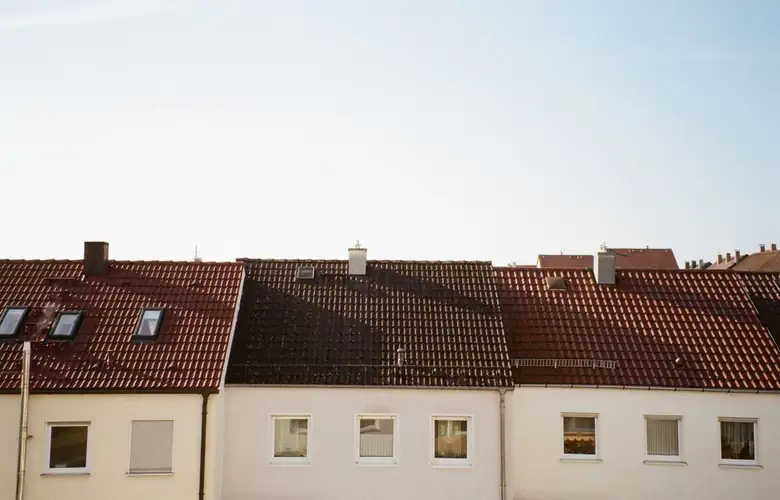 Red and brown tiled rooftops of suburban homes under a clear blue sky